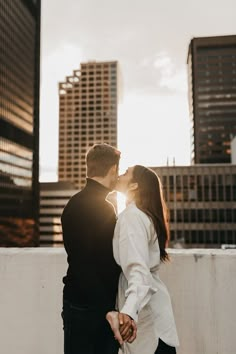 a man and woman standing next to each other in front of tall buildings with the sun shining down on them