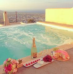 an outdoor pool with food and drinks on it, overlooking the cityscape in the background