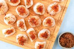 some kind of appetizer on a cutting board next to a bowl of seasoning