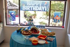 there is a birthday cake and other foods on the table in front of the window