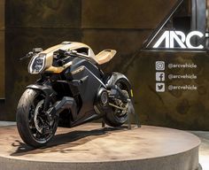 a black and gold motorcycle on display in front of an arce sign with information