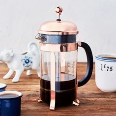 a coffee maker sitting on top of a wooden table next to cups and saucers