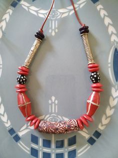 This one-of-a-kind necklace is made from an elbow Trade bead, various glass beads, antique silver long beads, and strung on red leather.  It has a bead at the end so that it can be adjusted to be shorter, by slipping the bead down.   These are beads are my favorites.  I've been collecting Trade beads for decades.  They were made mostly by Venetians in the 16th through the 20th centuries.  The black and white beads are called skunk beads and are also old.  I like to add pieces of antique silver f Red Necklaces With Silver Beads For Festival, Red Necklace With Silver Beads For Festival, Unique Red Beaded Necklaces For Festive Occasions, Red Artisan Beads For Festive Occasions, Festive Red Artisan Beads, Artisan Red Beaded Necklace With Dangling Beads, Artisan Red Dangling Beads, Red Wooden Beads For Festivals, Unique Red Necklaces With Dangling Beads