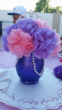 purple and pink flowers in a blue vase on a doily with a white lace tablecloth