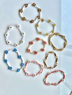 six bracelets with different colors and designs on white paper next to a pair of scissors