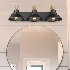 a bathroom mirror with three lights on it and a light fixture above the mirror that is black