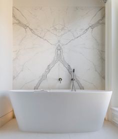 a large white bath tub sitting next to a window in a bathroom with marble walls and floors