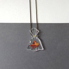 a goldfish in a bag necklace on a chain hanging from a hook with a white wall behind it