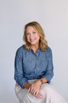 a woman sitting on top of a chair wearing a blue shirt and white pants with her legs crossed