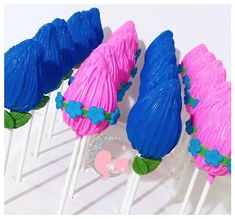 four blue and pink cake pops with green leaves on them, sitting next to each other