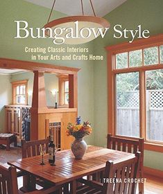 a dining room table with chairs and a vase on top of it in front of two windows