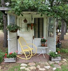 a yellow rocking chair sitting in front of a white shed with potted plants on it