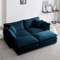 a large blue couch sitting on top of a white rug in a living room next to a window