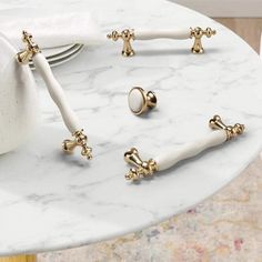 three white and gold handles on a marble table with place settings in the middle for napkins