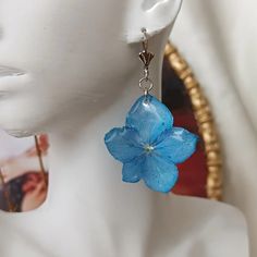 a pair of blue flower earrings hanging from a mannequin head