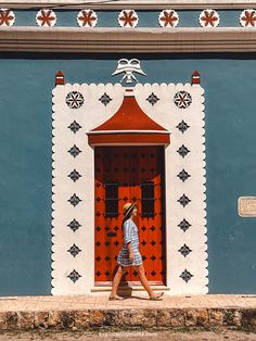 a woman walking in front of a blue and white building with an orange door on it