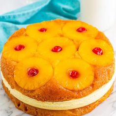 a cake with pineapples on top is sitting on a marble surface next to a glass of milk