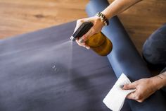 a person is cleaning the floor with a rag and bottle in their hand while sitting on an exercise mat