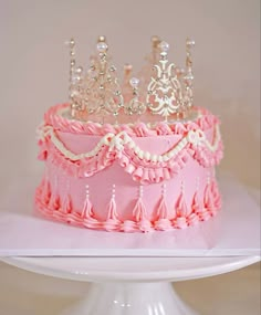 a pink and white cake with a tiara on top is sitting on a pedestal