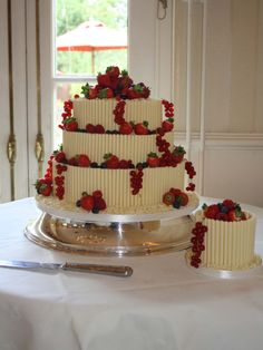 a three tiered cake with strawberries and berries on top sits on a table