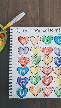 a child's art project with letters and hearts painted on paper next to a bowl of fruit