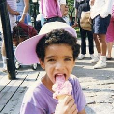 a young boy wearing a pink hat eating an ice cream cone