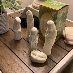 three white statues sitting on top of a wooden table next to a box and potted plant