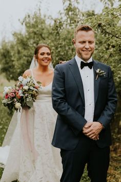 a bride and groom standing in an apple orchard