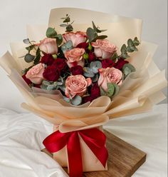 a bouquet of roses is wrapped in brown paper and tied with a red ribbon on a wooden board