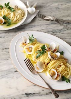 pasta with clams and parsley on white plate next to silverware, fork and spoon