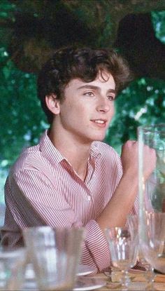 a young man sitting at a table with many empty glasses and plates on the table