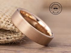 two gold wedding bands sitting next to each other on a wooden table with burlock