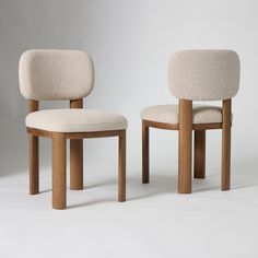 two wooden chairs sitting next to each other on a white surface with one chair facing the other