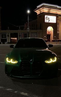 a green sports car parked in front of a building at night with its lights on