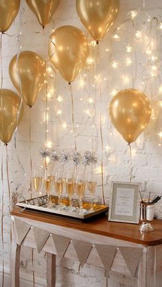 a table topped with lots of balloons and champagne glasses next to a white brick wall