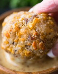 a close up of a person holding a food item in front of a bowl filled with sauce