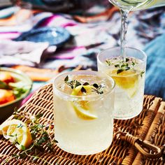 two glasses filled with lemonade sitting on top of a woven place mat next to a bowl of fruit