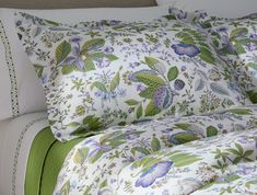 a bed covered in green and white sheets with flowers on it's headboard