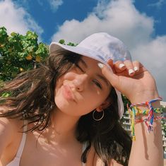 a woman wearing a white hat and holding her hand up to her face while standing on the beach