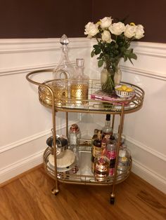 a gold bar cart with drinks and flowers in it on the floor next to a wall