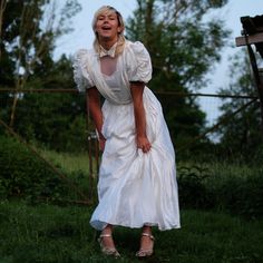 a woman in a white dress is standing on the grass with her hands behind her back