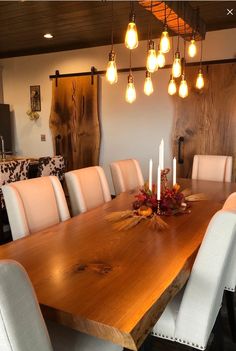 a large wooden table with white chairs and lights hanging from it's ceiling in a dining room