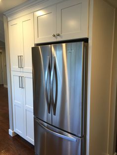 a stainless steel refrigerator in a kitchen with white cabinets and wood flooring on the walls