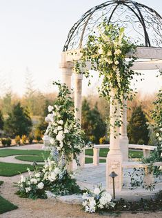 an outdoor wedding ceremony setup with white flowers and greenery on the arbor, in front of a circular gazebo