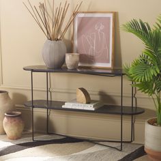 a shelf with books and vases on it next to a potted palm tree