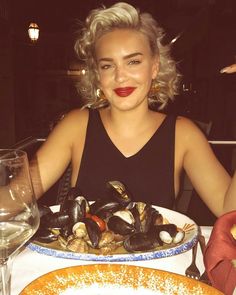 a woman sitting at a table with a plate of clams in front of her