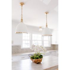 a kitchen with two hanging lights over the island and flowers on the table in front of it