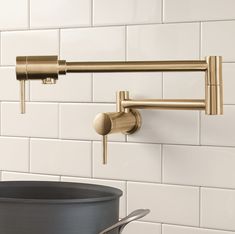 a brass faucet is mounted on the wall above a black pot and white tiles