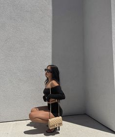 a woman sitting on the ground with her legs crossed, wearing sunglasses and holding a purse