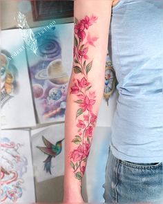 a woman's arm with pink flowers on it and a humming flying over her shoulder